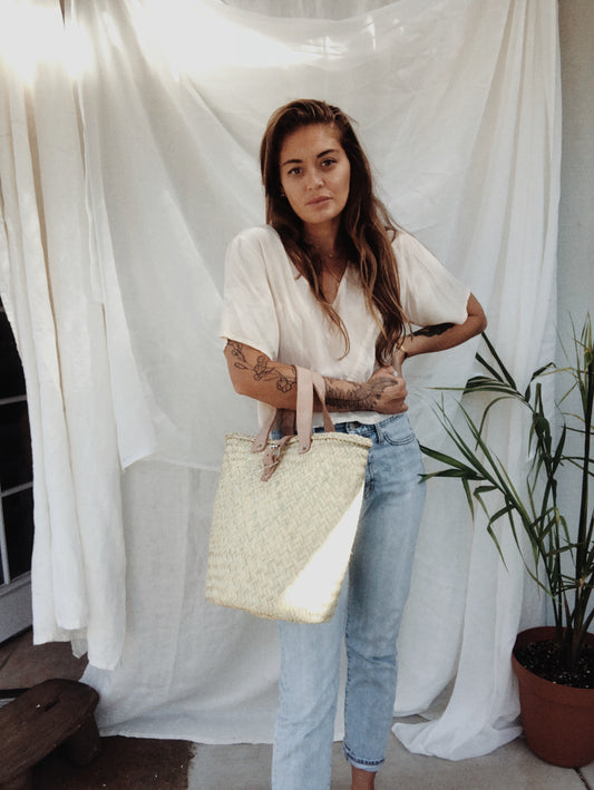 model holding a rattan woven bag with leather handles and a leather buckle closure